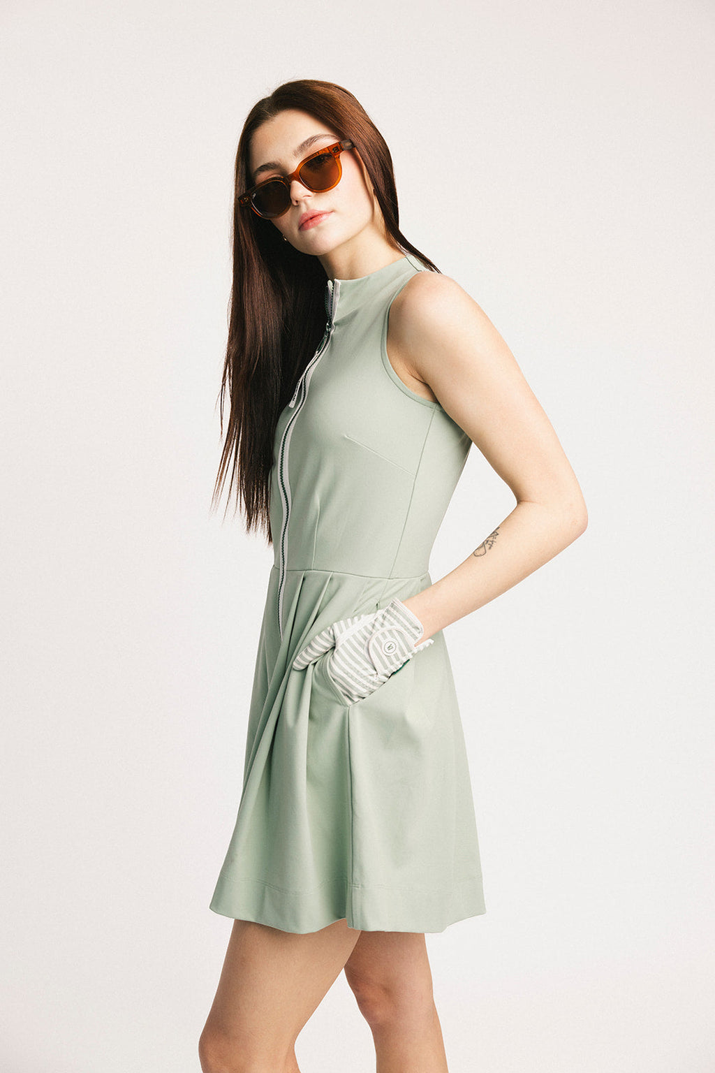Woman wearing a light green dress and sunglasses on a plain background