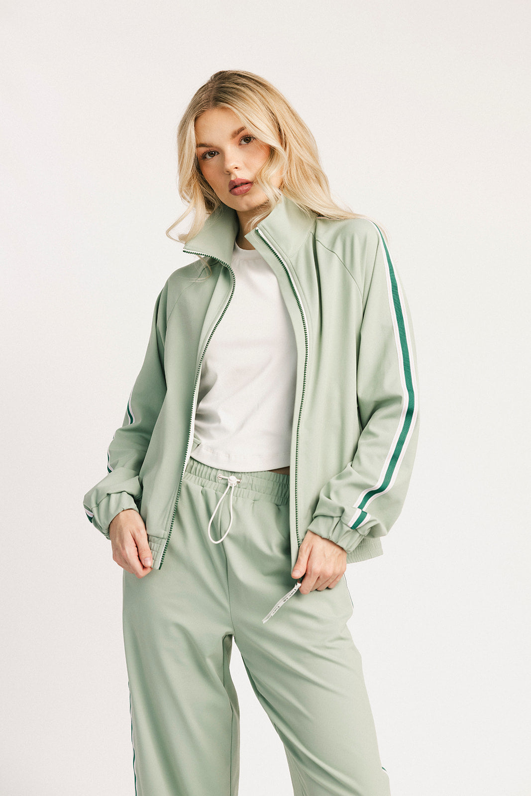 Woman wearing a light green tracksuit with a white top on a white background