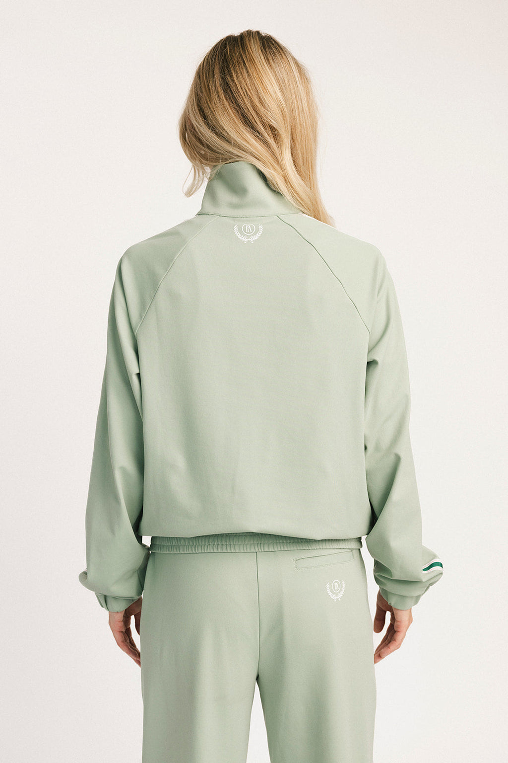 Person wearing a light green tracksuit with a brand logo on a white background